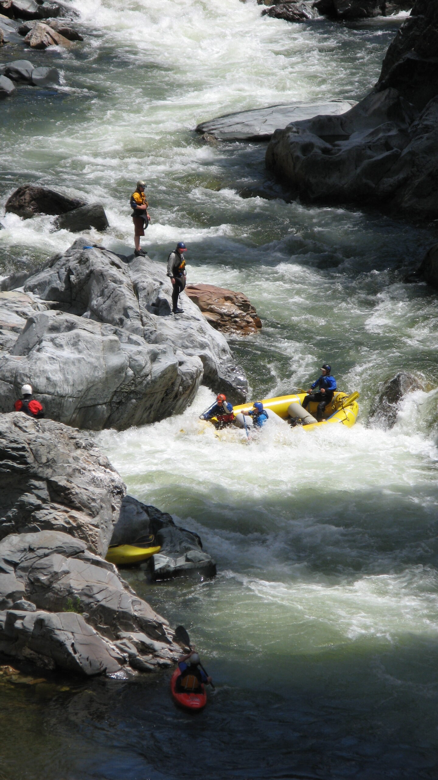 rafters on a rapid with some guides standing on rocks above checking out what they are doing