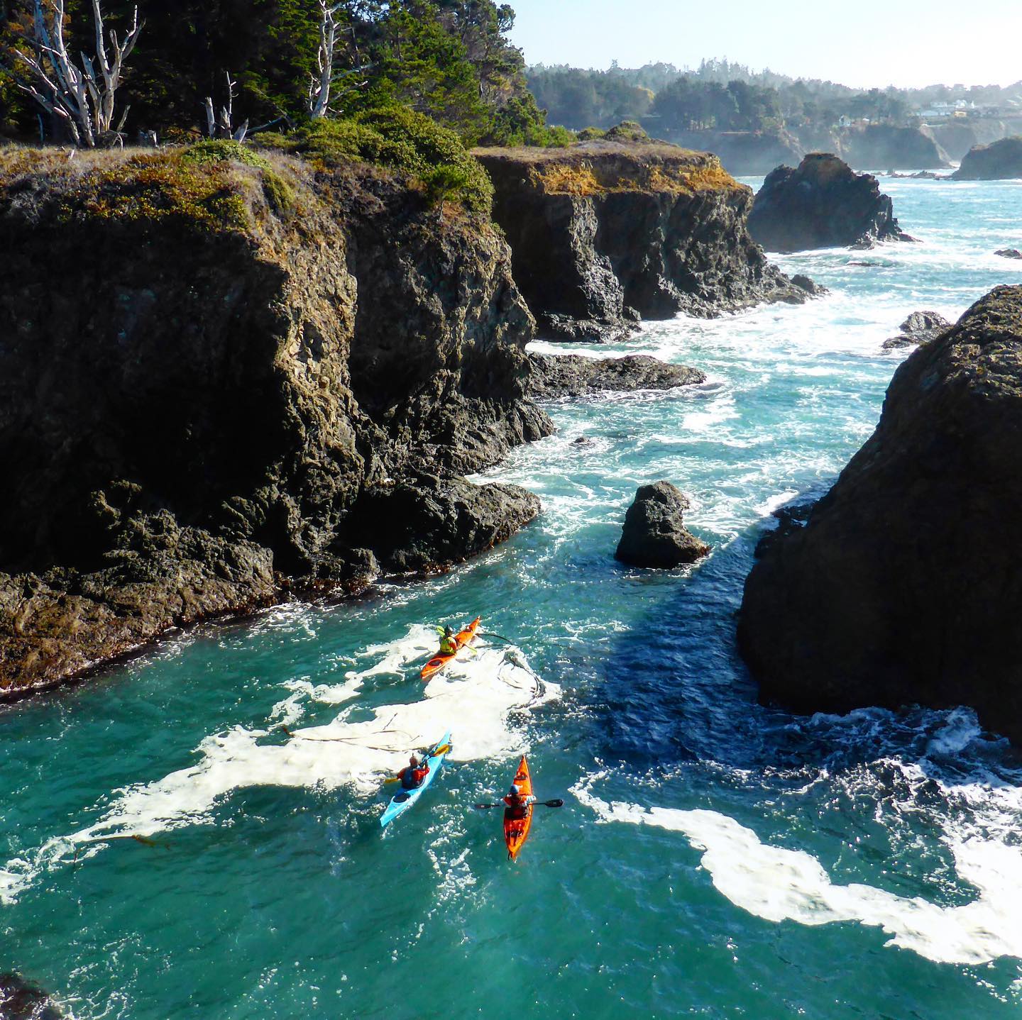 Photo of kayakers in Mendocino, Californi. They are paddling through blue water with cliffs on both sides