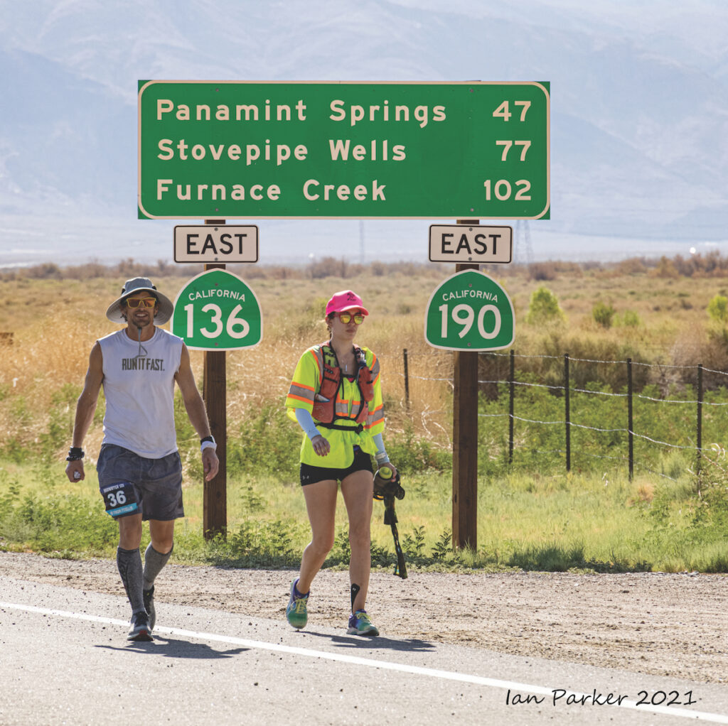Badwater runners walking under a road sign in the heat.