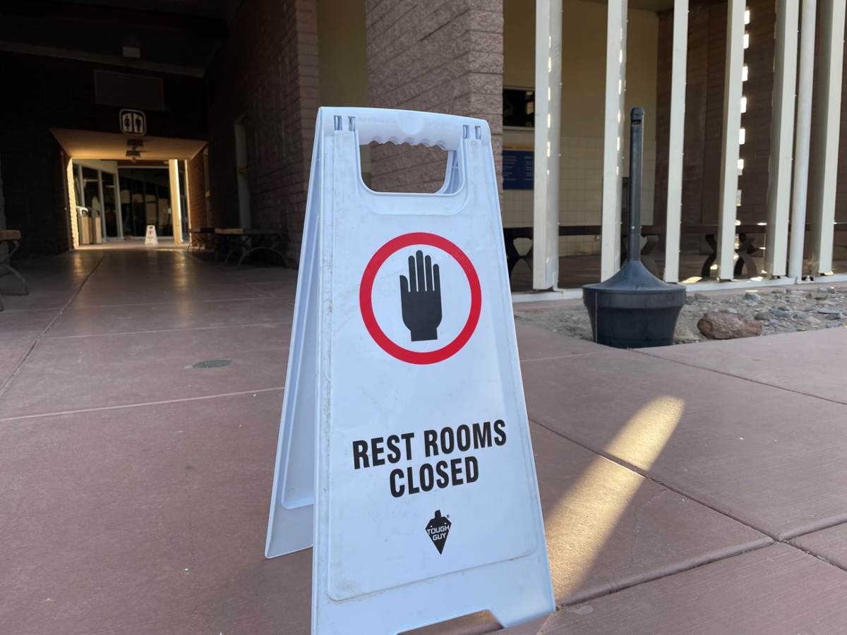  A white temporary A-frame sign shows a hand in a red circle and reads, "Restrooms closed". This sign is placed at Furnace Creek Visitor Center when the water system is broken.